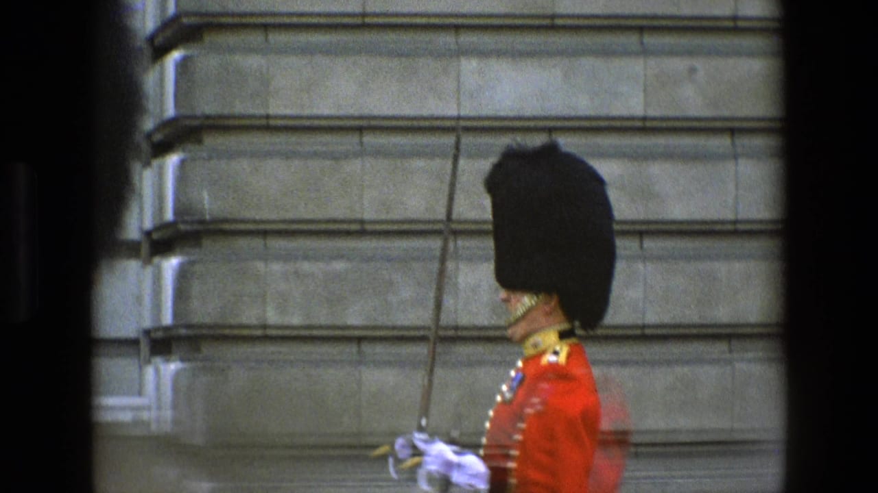 1969 England footage showing a ceremonial guard in red uniform, tall black headdress, white gloves, and sword beside a grey stone wall.