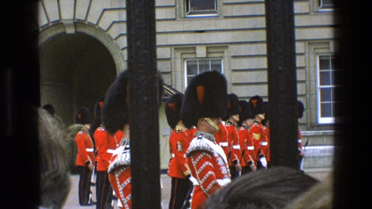 1969 Buckingham Palace footage shows Queen's Guard soldiers with bearskin hats, rifles, and white belts standing in formation, with a palace arch and windows behind them.