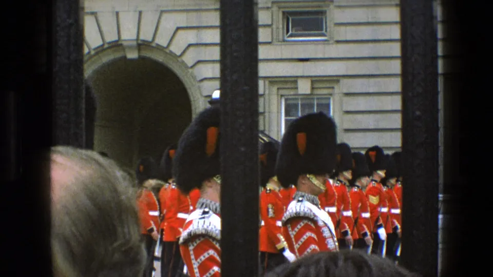 Final 1969 London frame shows Queen's Guard soldiers in red ceremonial dress at Buckingham Palace, with vertical bars and spectators partially obstructing the home-movie view.