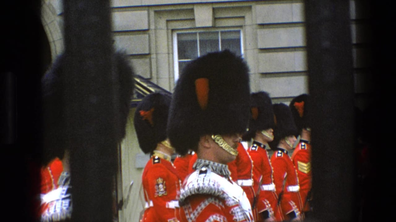 Close home-movie view of Grenadier Guards in ceremonial uniforms outside Buckingham Palace, with dark bars cutting through the frame.