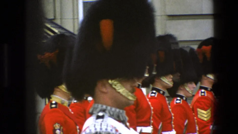 1969 England home-movie frame of Queen's Guard soldiers in ceremonial uniform, seen from a crowded or obstructed spectator angle.