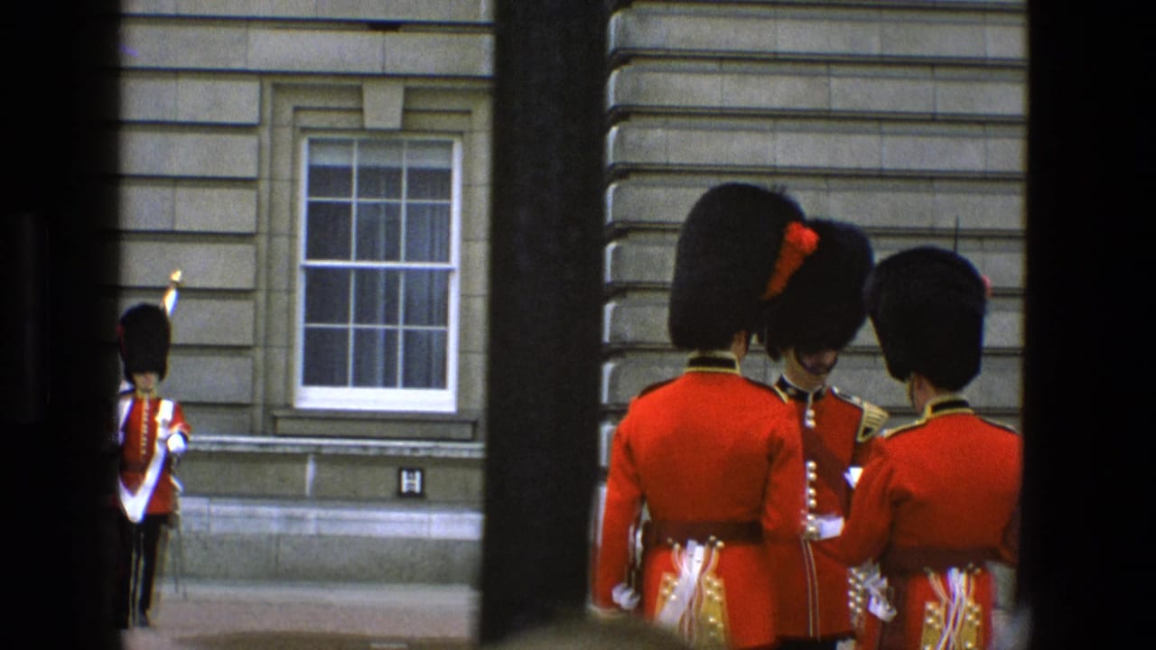 Royal guards in red tunics stand near a palace facade behind dark gate bars.