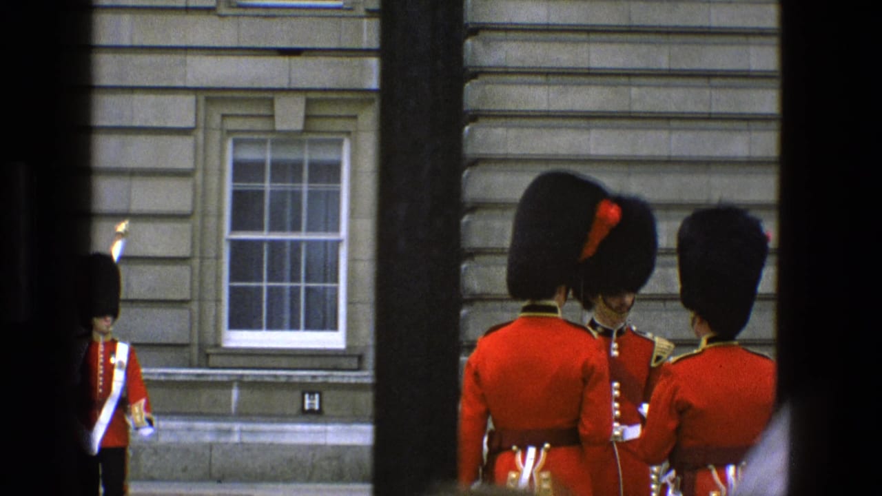 Ceremonial guard in red tunic stands near a stone building, partly blocked by dark foreground bars.