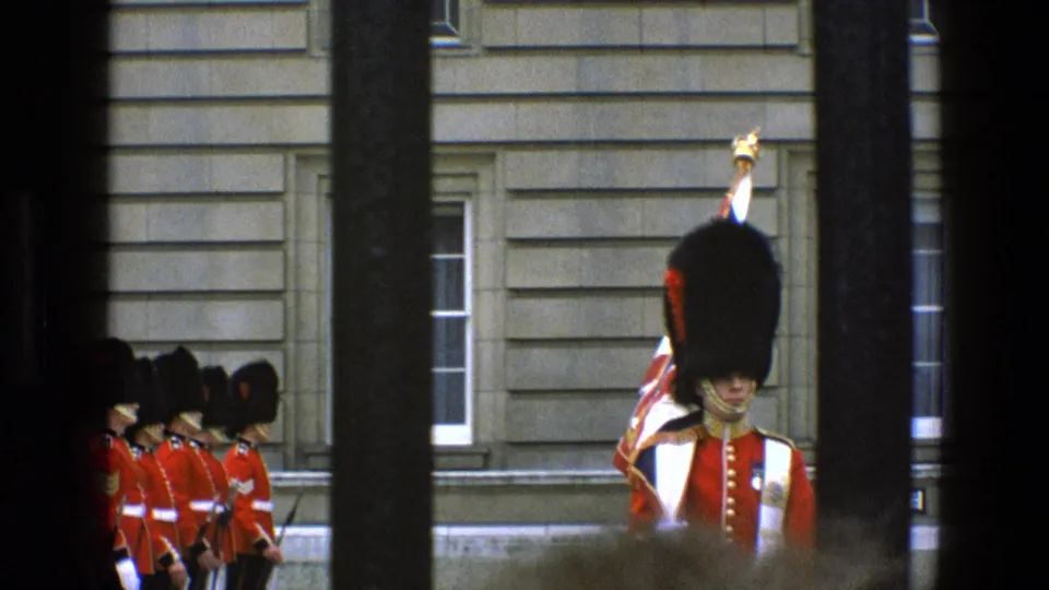 1969 England frame showing a guard with a raised ceremonial staff or standard, with other guards lined along the left side.