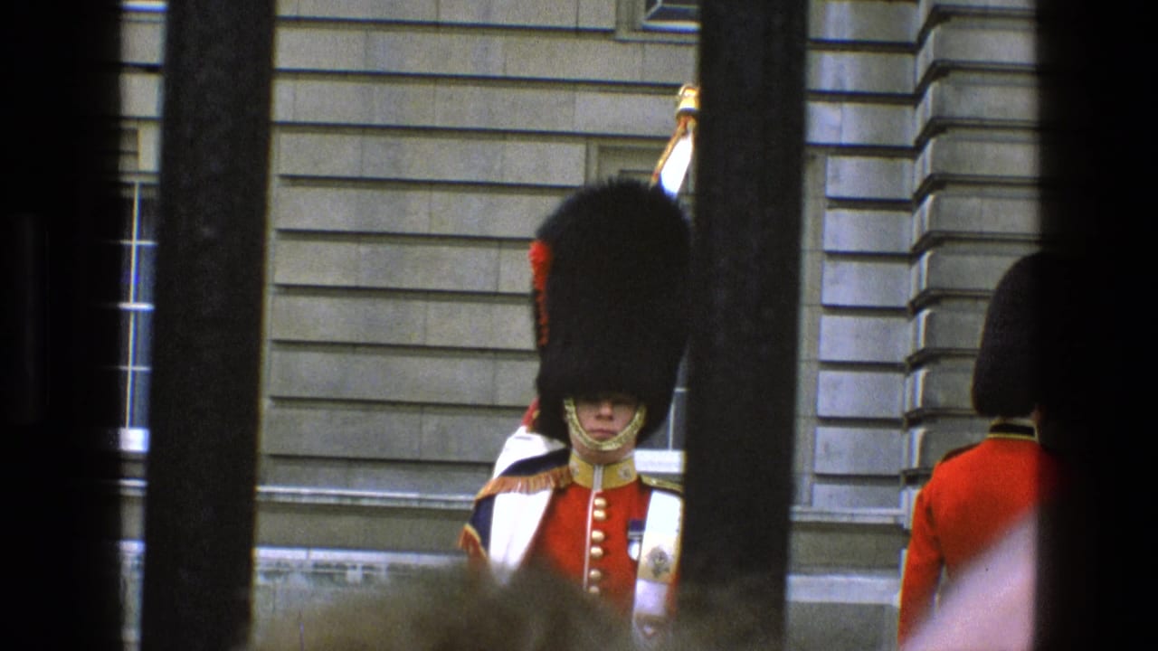 1969 England 8mm frame showing a royal guard in red tunic and bearskin hat viewed through dark gate bars.