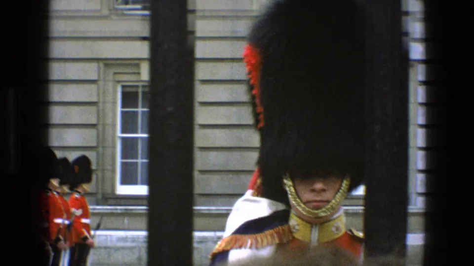 1969 England 8mm frame with a close royal guard behind bars and additional guards standing near the building.
