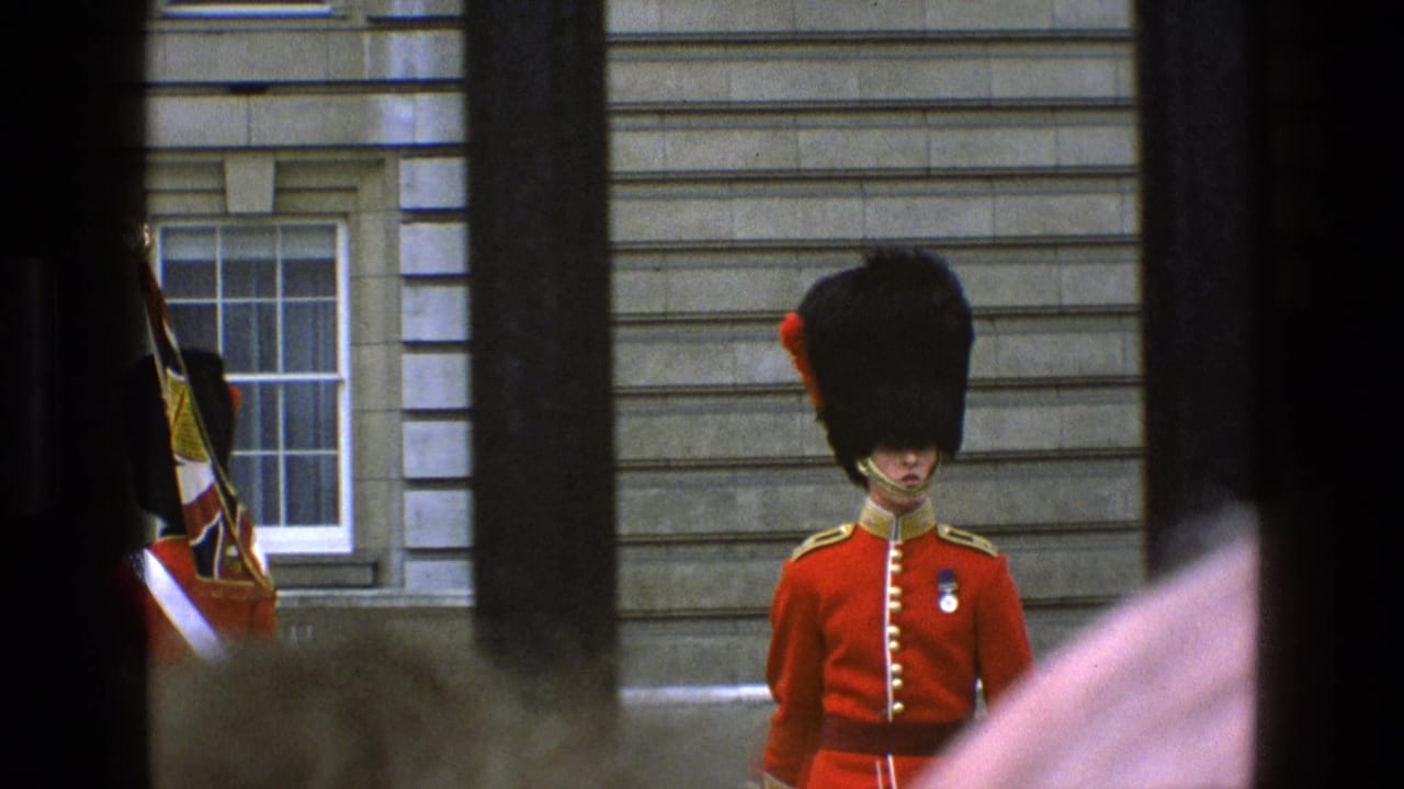 Guard in red uniform stands at attention outside a stone building.