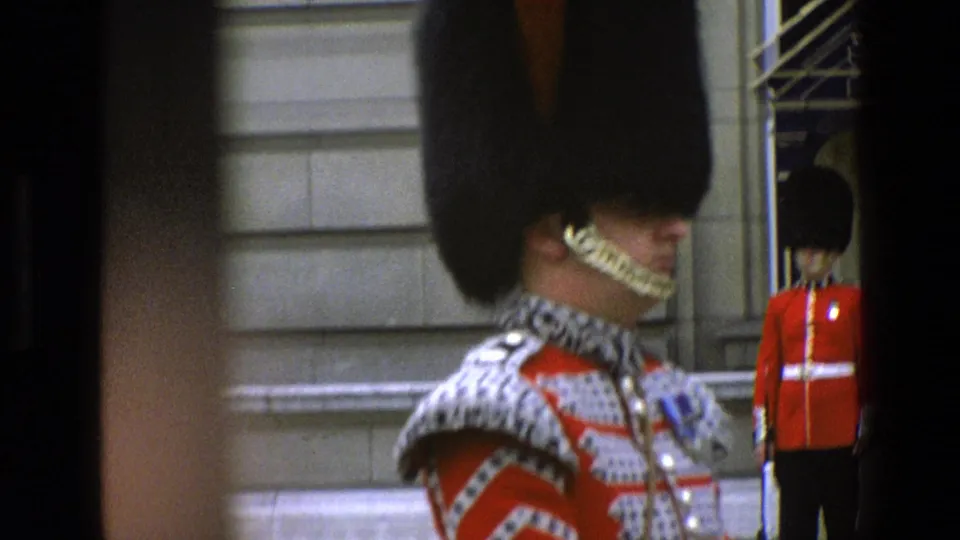 Soft 8mm close view from 1969 England showing a ceremonial guard in red and silver uniform, with another guard standing by a doorway behind him.