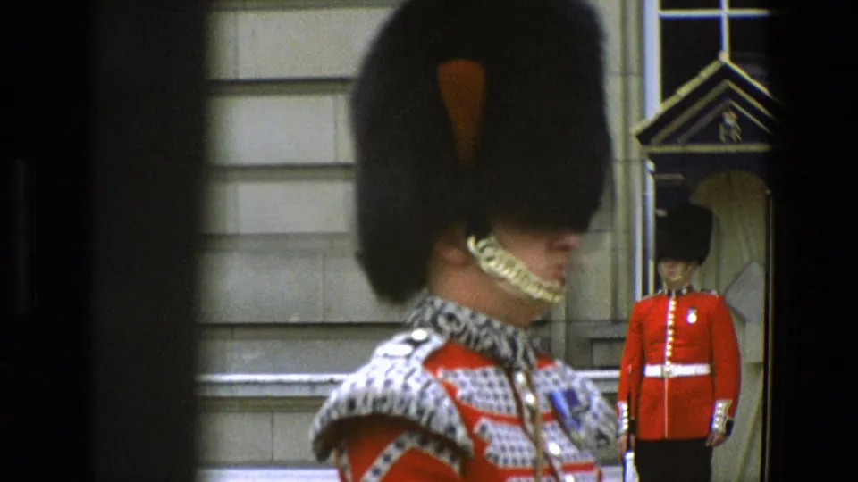 1969 England frame showing a close ceremonial guard in bearskin hat and red tunic, with another guard standing in the background by a stone doorway.