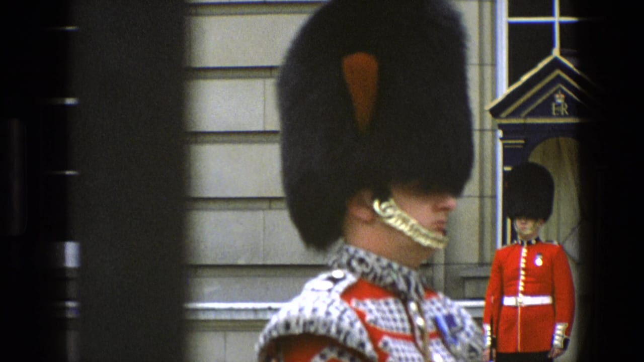 1969 England home-movie frame showing a Grenadier Guard in foreground at Buckingham Palace with a second sentry in the background.