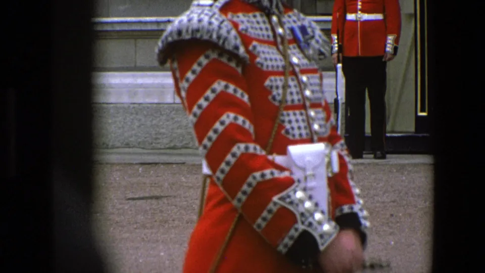 Visitor-shot 8mm frame of a Grenadier Guard in profile at Buckingham Palace, with ceremonial uniform details and a rear sentry visible.