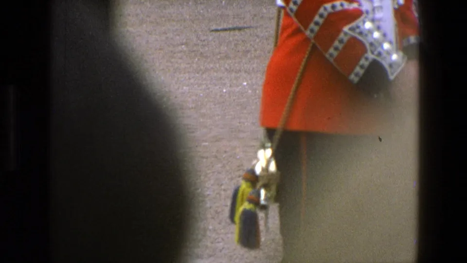 A red-uniformed ceremonial guard is cropped at the torso, with staff and brass ornament visible in soft 8mm color.