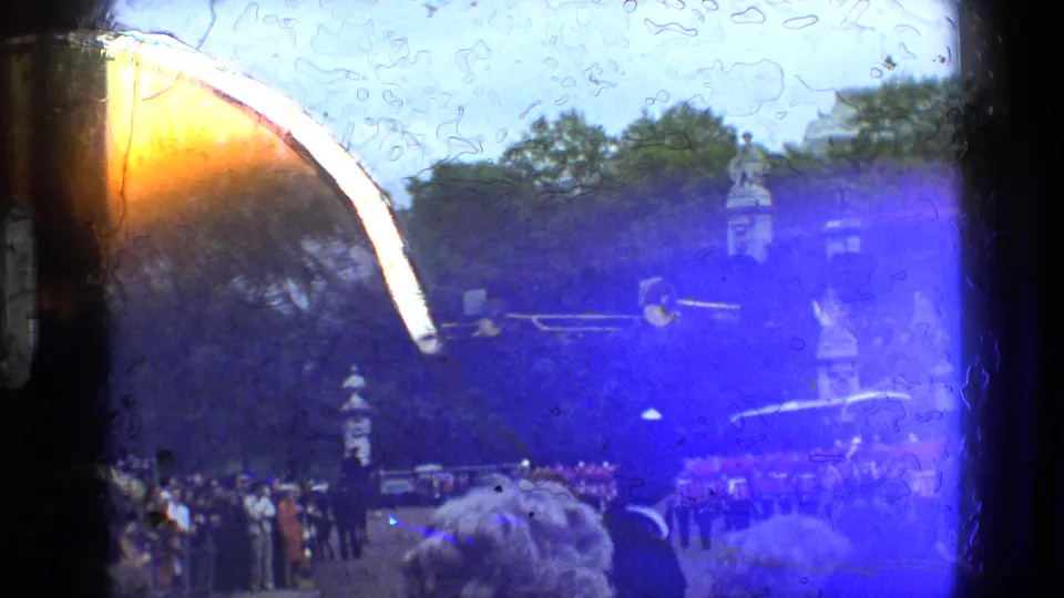 Spectators watch the guards band from the side of the parade ground, with a strong blue and orange 8mm light leak across the frame.