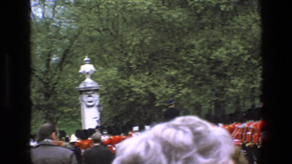 1969 England frame showing spectators' heads in the foreground as ceremonial guards march near a stone pillar and trees.