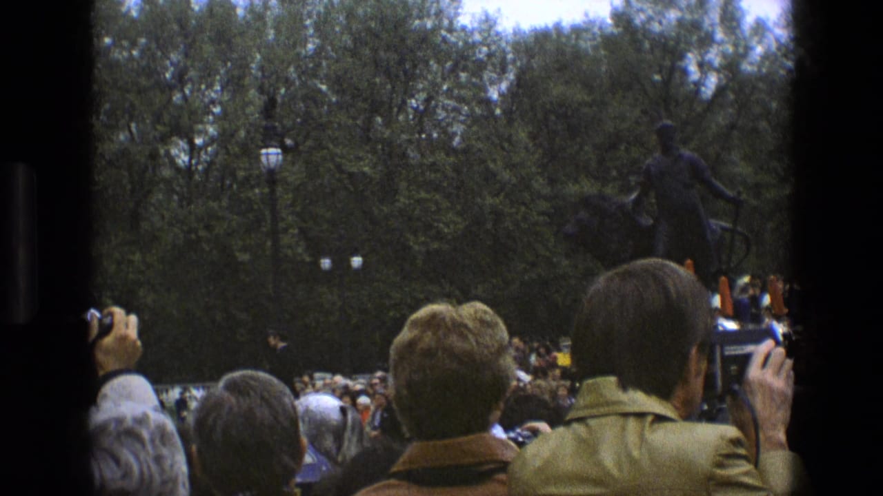 1969 England 8mm frame showing spectators from behind as uniformed guards pass in a park-like ceremonial setting.