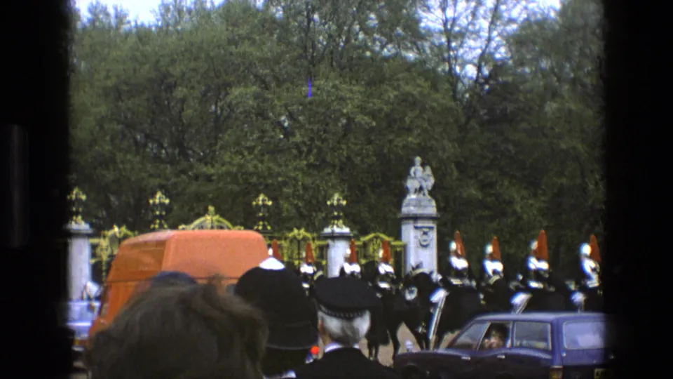 1969 England 8mm frame showing ceremonial guards in formation near ornate gates, with spectators and cars in front.