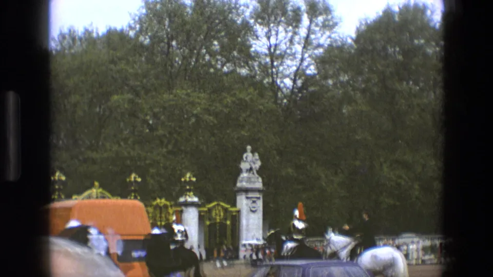 1969 England frame with mounted ceremonial guards, horses, an orange van, railings, trees, and spectators near a royal London landmark.