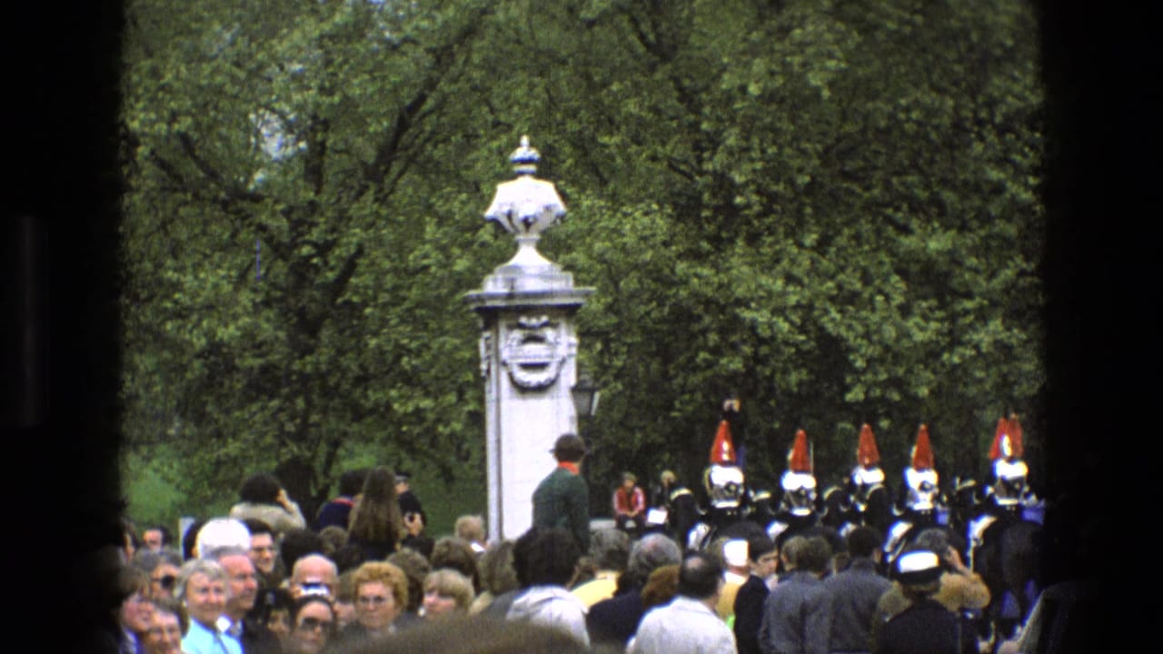 Spectators face mounted guards beside a white pillar and trees.