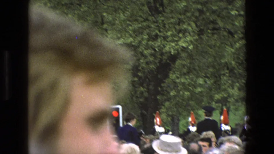 Handheld 8mm frame from England in 1969, with a blurred spectator close to camera and ceremonial guards beyond the crowd.
