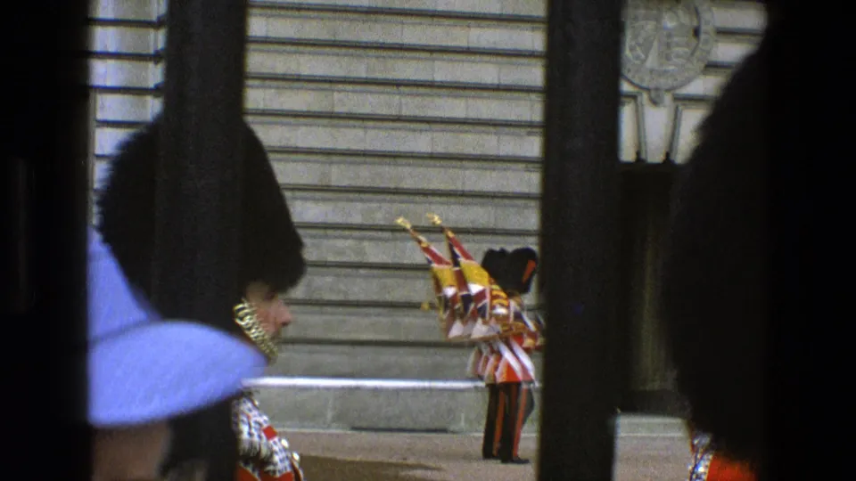 1969 England parade view with guards in bearskin hats, a Union Jack flag, and spectators partially blocking the frame.