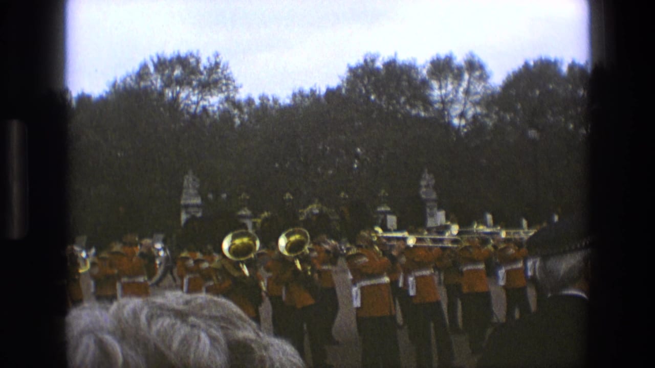 Brass band members in orange uniforms stand outdoors with trees behind them.