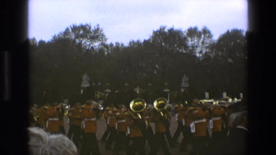 Handheld 8mm frame from England in 1969 showing orange-uniformed musicians performing on a grassy outdoor area.