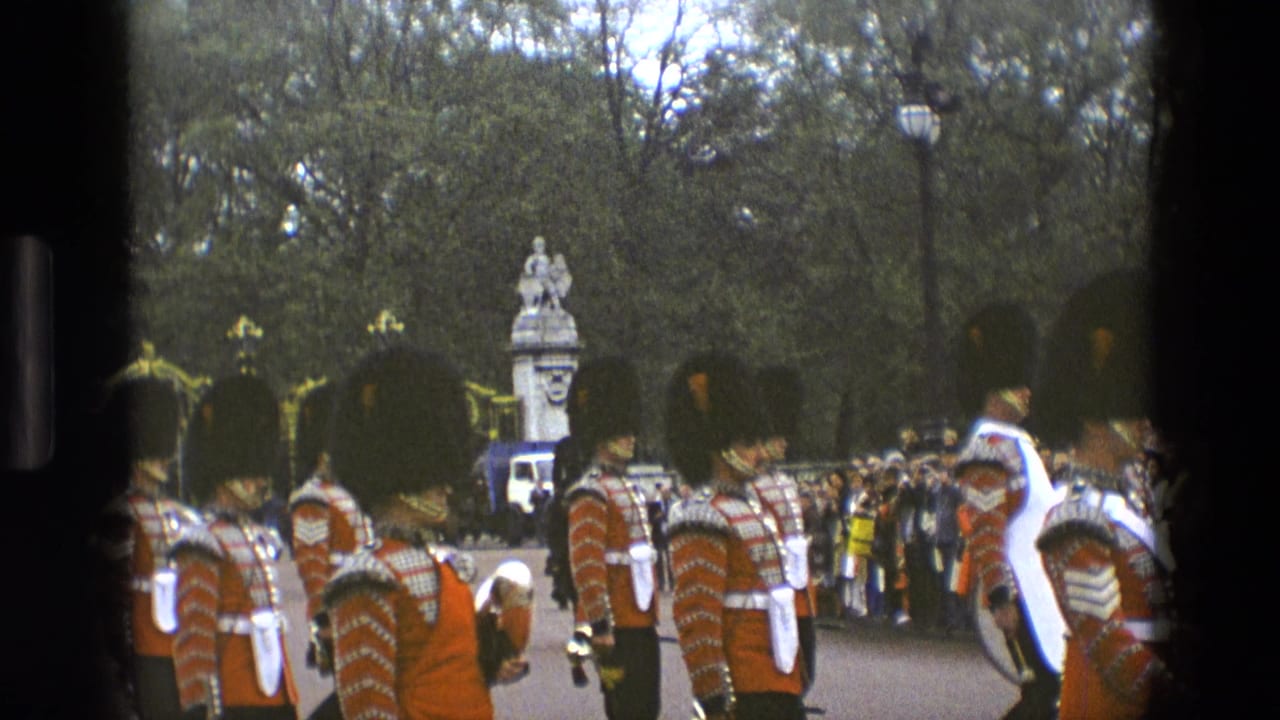 1969 England home-movie frame with uniformed guards in bearskin hats moving in formation as a crowd watches from the roadside.