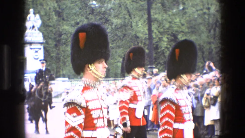 1969 England 8mm frame showing a closer side view of guards in ceremonial uniform, with a mounted officer and crowd in the background.