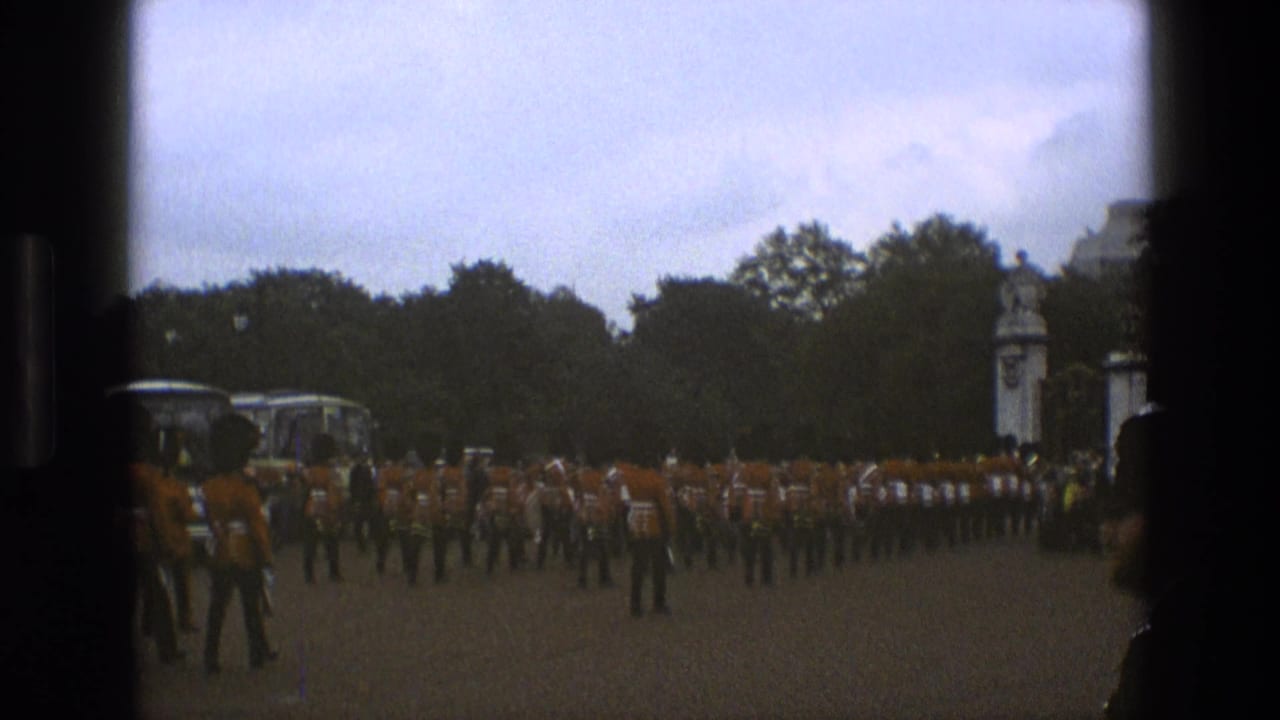 A 1969 England frame shows rows of uniformed marchers in red-orange tunics moving in formation near trees and white gate posts.