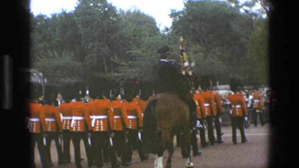 1969 England frame showing a mounted officer, horse, flags, and British guards in red ceremonial uniforms within a park-like setting.