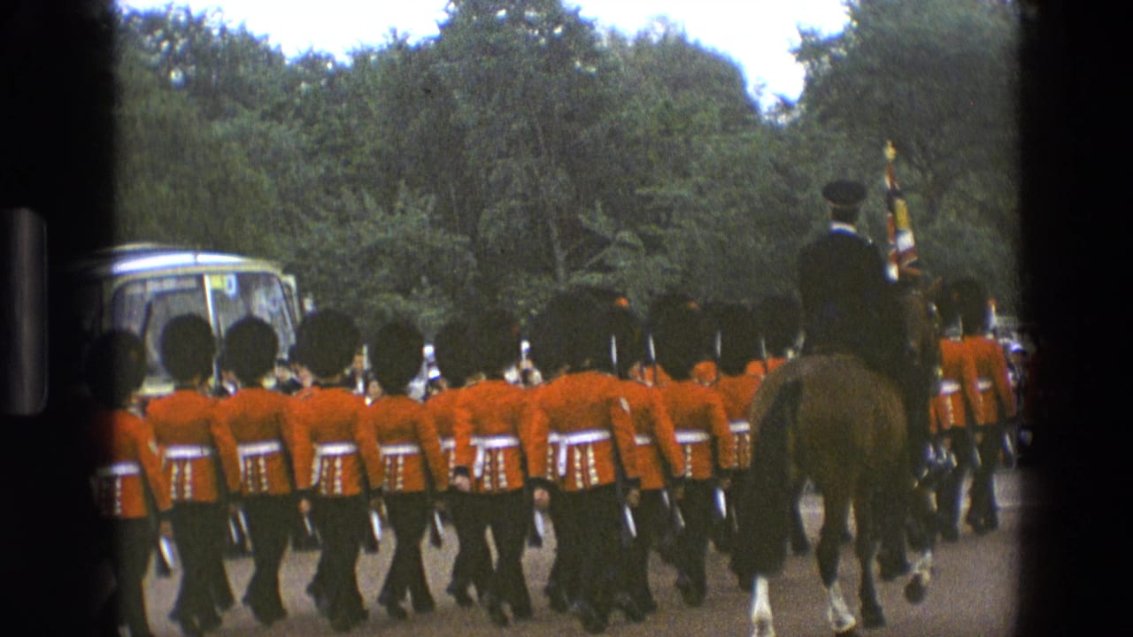 Marching guards in red tunics follow a mounted officer on a tree-lined road.
