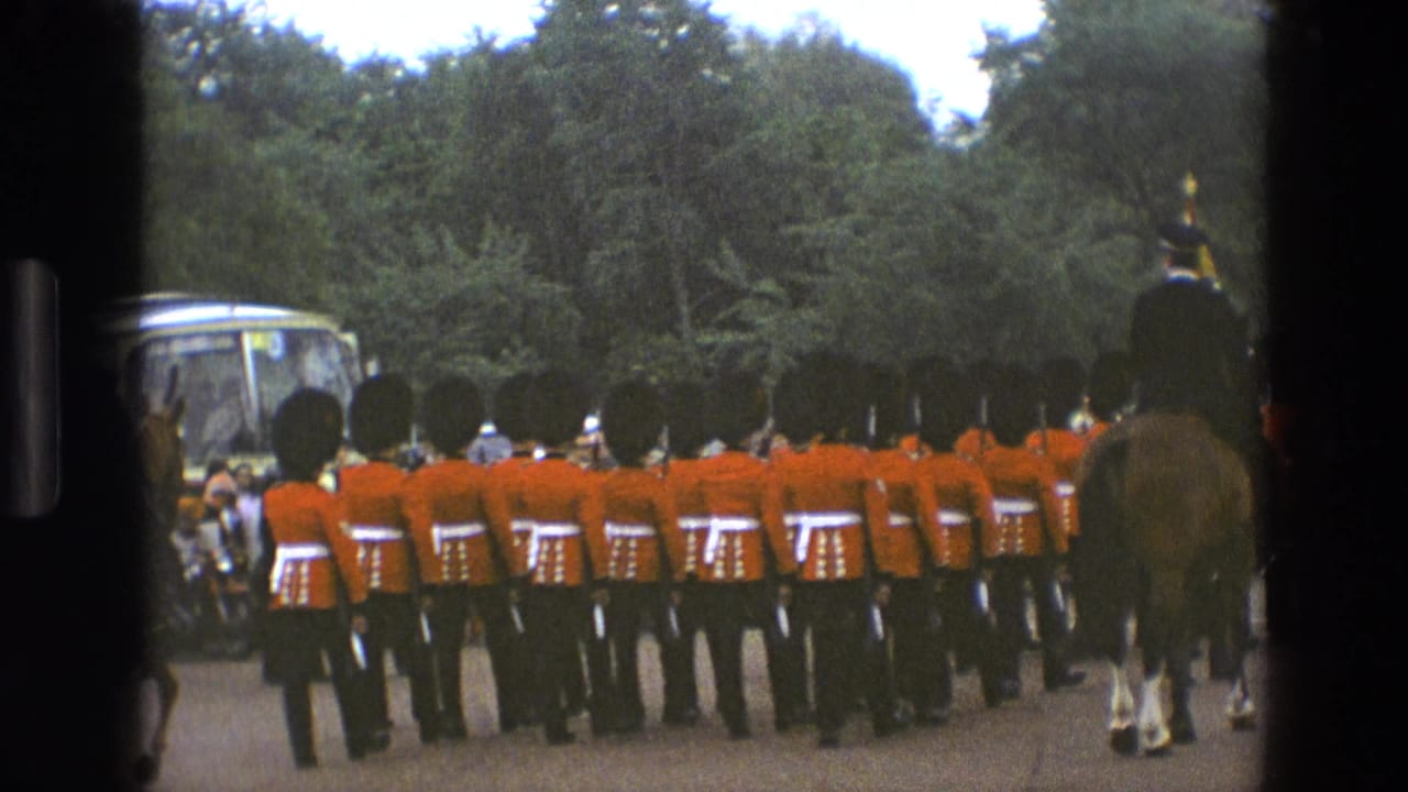 Formation of guards in red uniforms marches away with a mounted officer at right.
