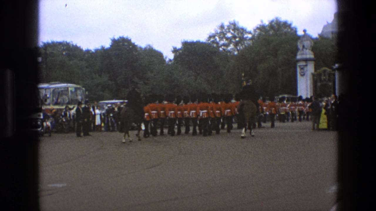 1969 England 8mm frame with guards in red coats, mounted riders, a spectator crowd, trees, formal gates, and a coach in the background.