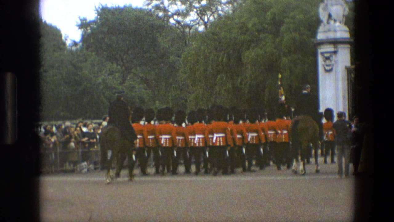 1969 England footage frame with marching guards, mounted escorts, spectators behind barriers, trees, and a stone pillar at the parade ground edge.