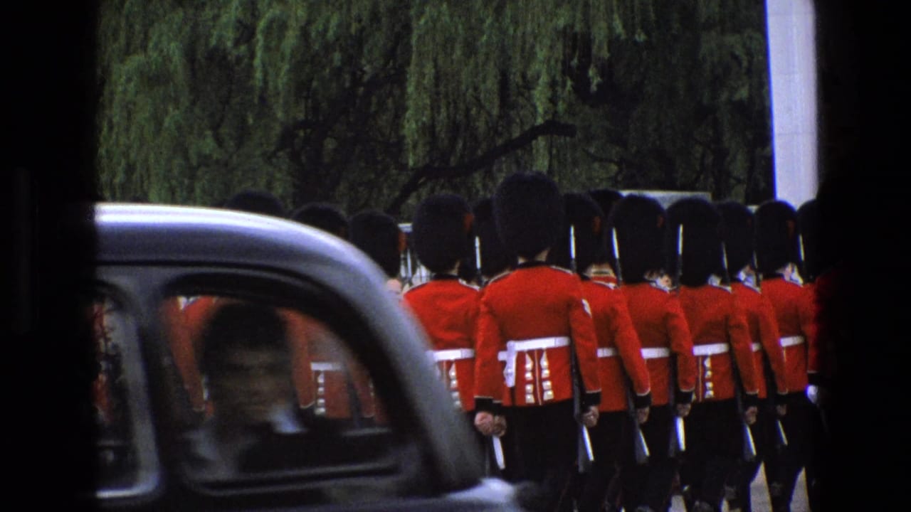 1969 England home-movie frame with red-uniformed guards marching as a black taxi passes across the foreground.