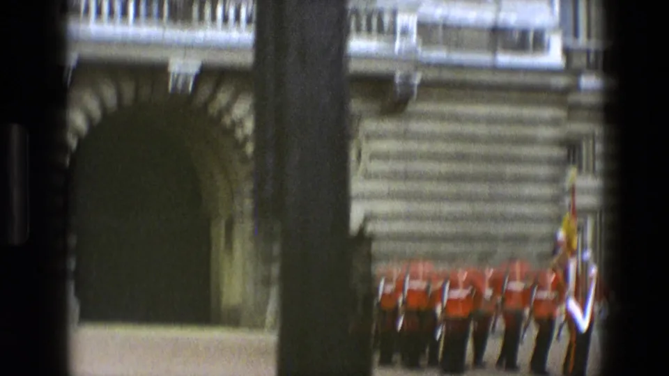 1969 England 8mm frame with motion-blurred ceremonial guards near a stone arch, seen through dark foreground bars.