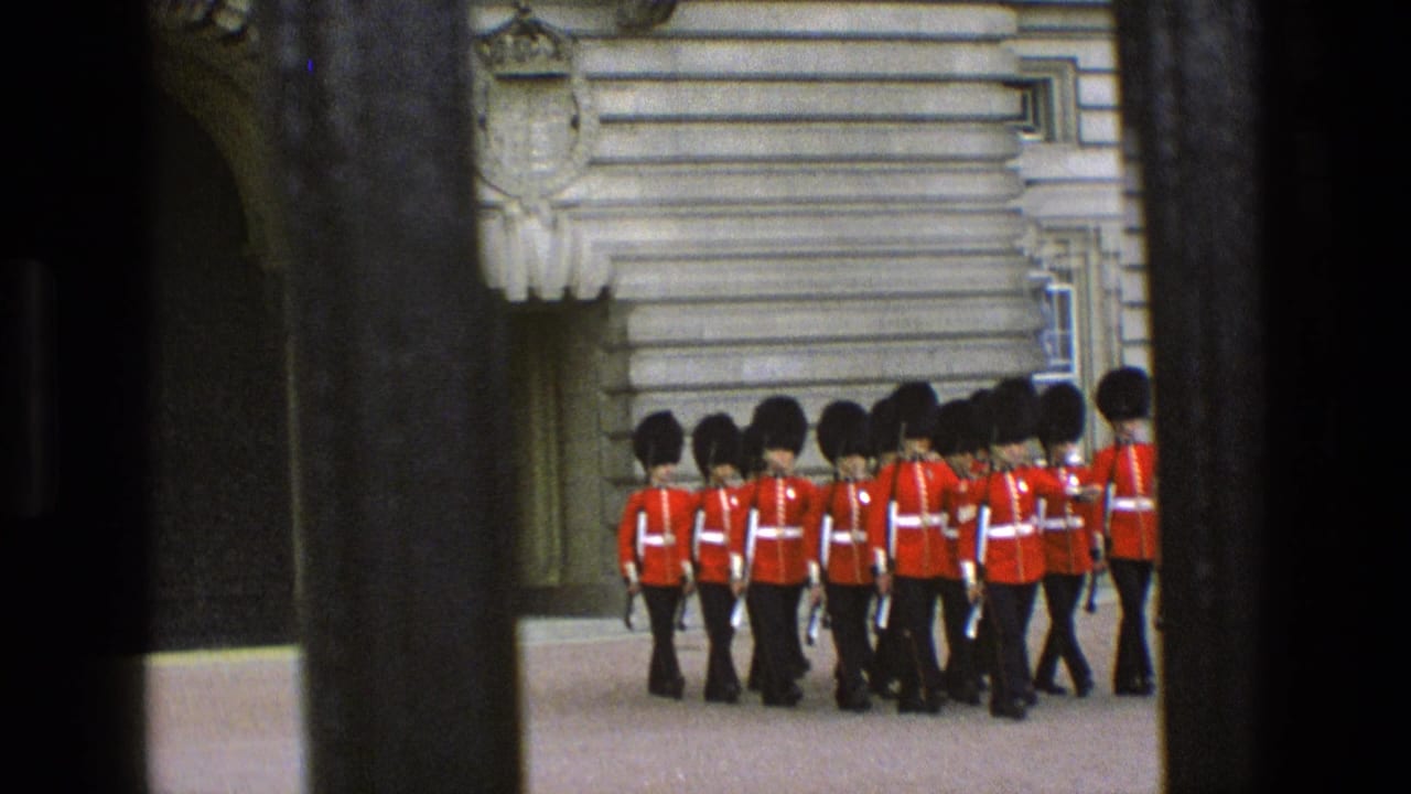 Buckingham Palace guards in red tunics march behind dark vertical railings.