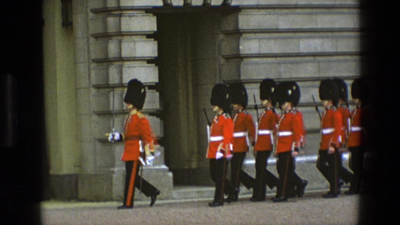 Guards in red uniforms march past stone palace architecture.