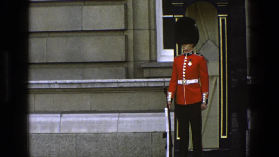 1969 visitor-shot footage shows a ceremonial guard in red uniform at his post, with a rifle, dark doorway, and stone building details visible.