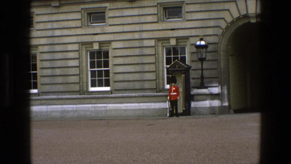 1969 England visitor-shot frame with a distant ceremonial guard by a sentry box near windows and an arched entrance.