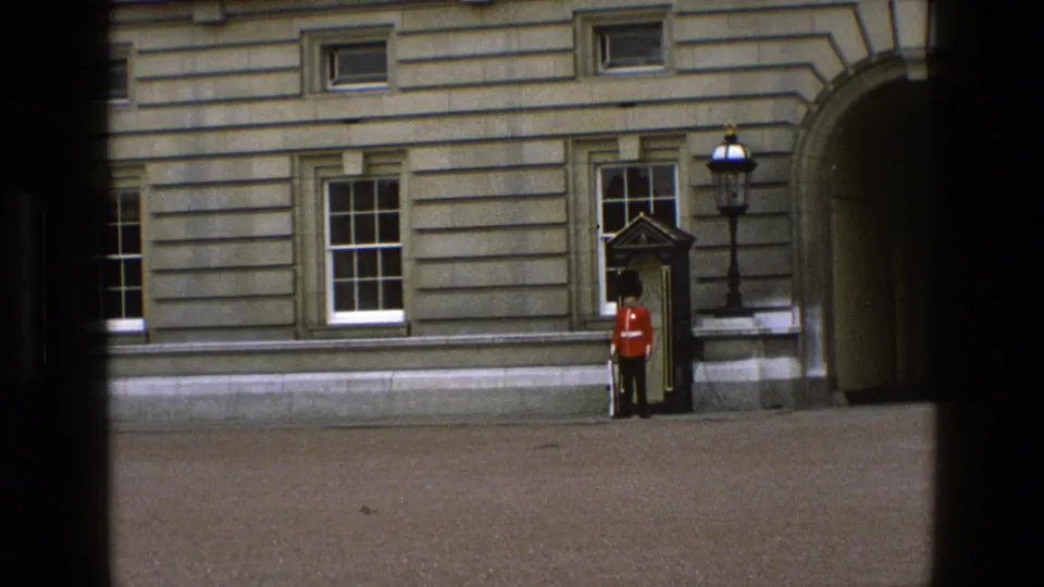 1969 England 8mm frame showing a ceremonial guard and sentry box against a large stone building, partly obscured by dark framing.