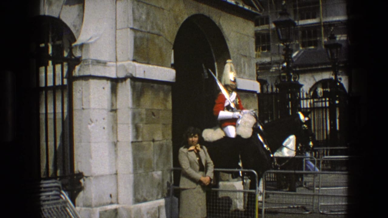 1969 England frame of a ceremonial rider on a black horse near iron gates, with a civilian woman in view.