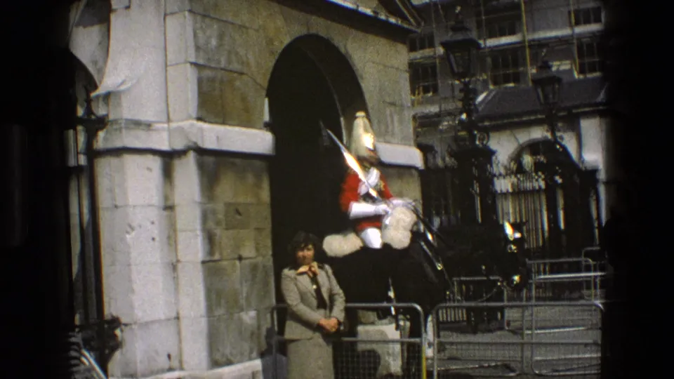 1969 England frame showing a mounted ceremonial guard at a historic stone gate with a woman standing close by.