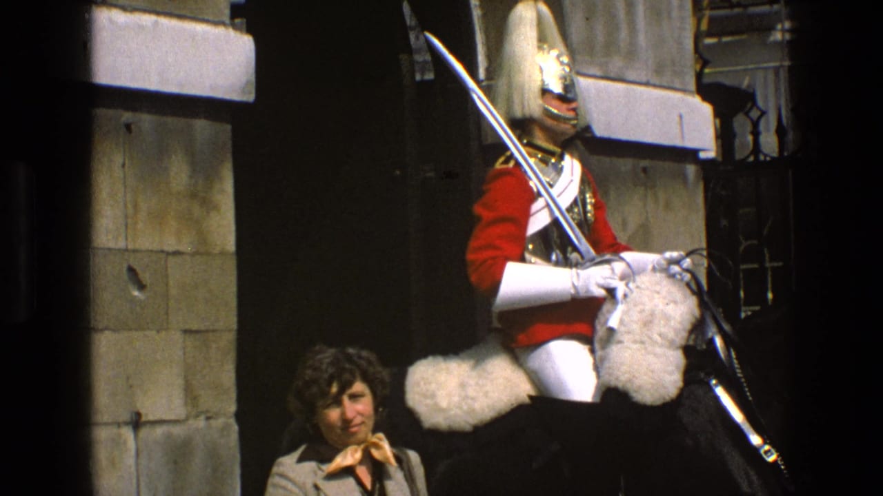 In England, 1969, a tourist woman stands near a mounted guard in red ceremonial uniform holding a sword at a stone gate.