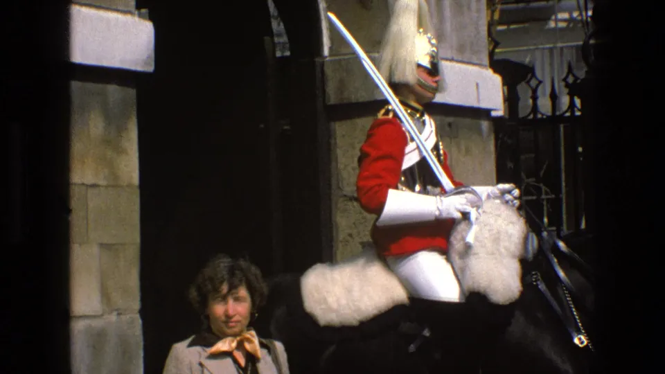The tourist woman appears below the mounted guard, whose red uniform, white tack, sword, and black horse dominate the frame.
