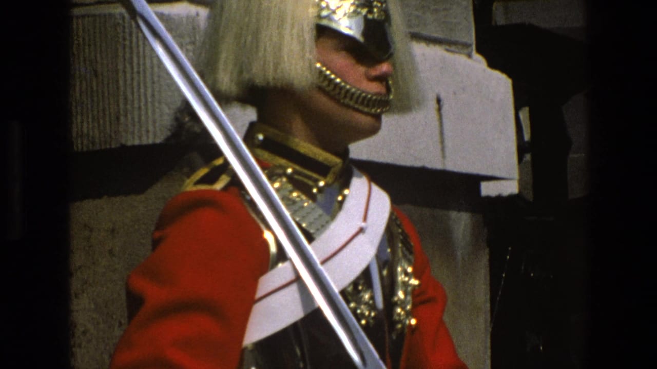 Ceremonial guard in plumed helmet and red tunic stands beside a stone wall with saber raised.