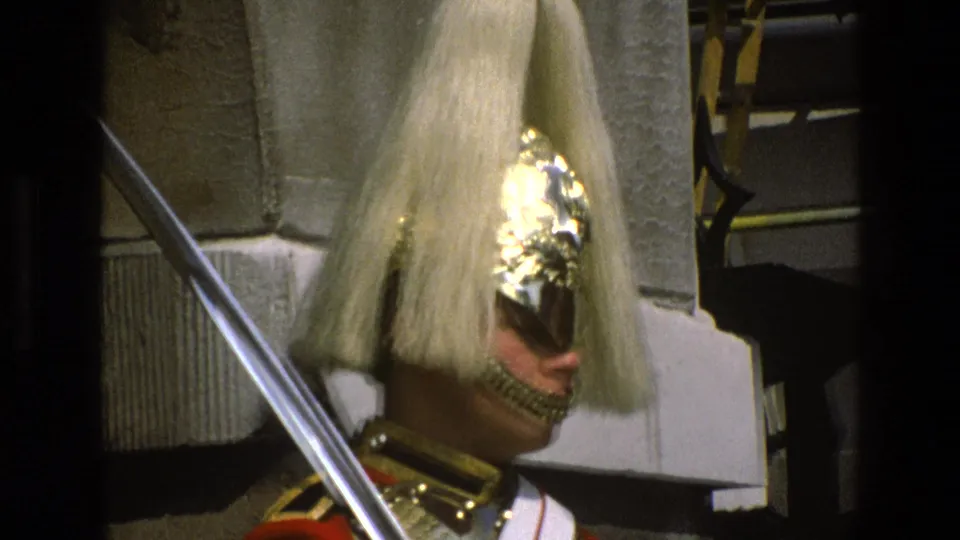 Final 1969 England frame focusing on the ceremonial guard's tall plume, reflective helmet front, saber, and red tunic.
