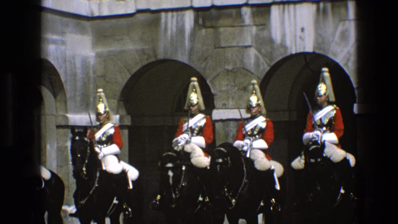 Four mounted ceremonial riders in red uniforms sit on black horses before stone arches.