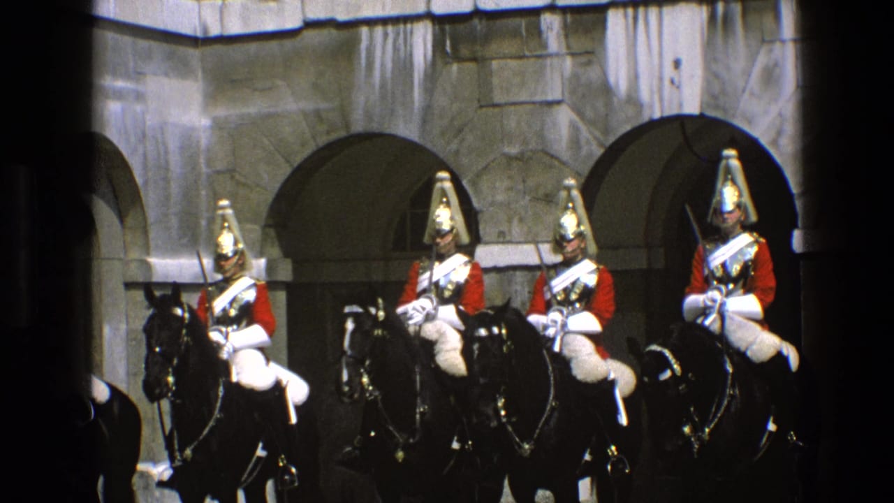 Mounted riders in red ceremonial dress remain lined up in front of arched stone openings.