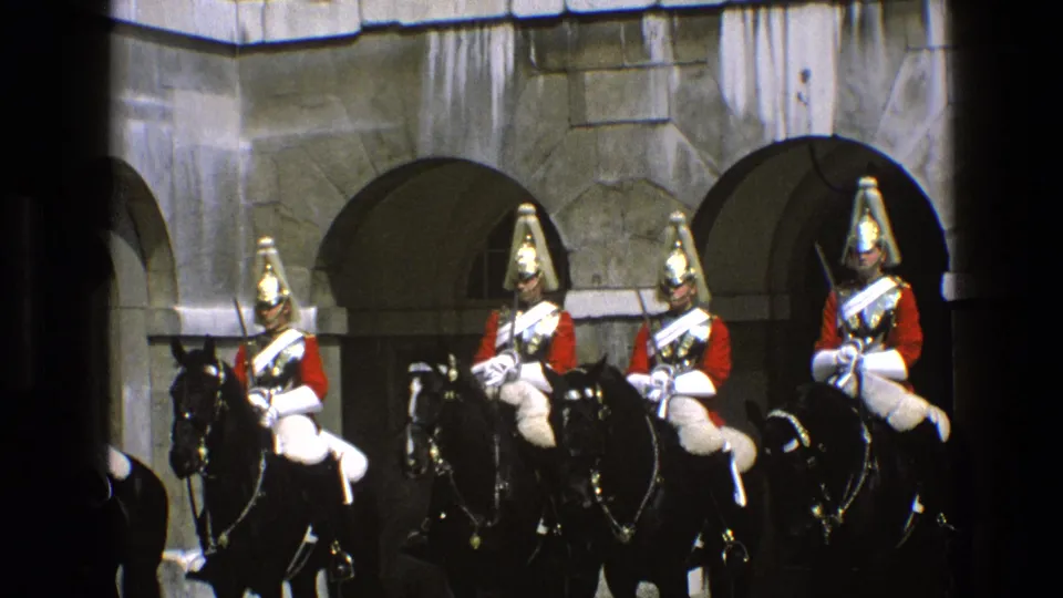 Four riders on black horses wear red coats, white crossbelts, and tall helmets in a 1969 England ceremonial guard scene.